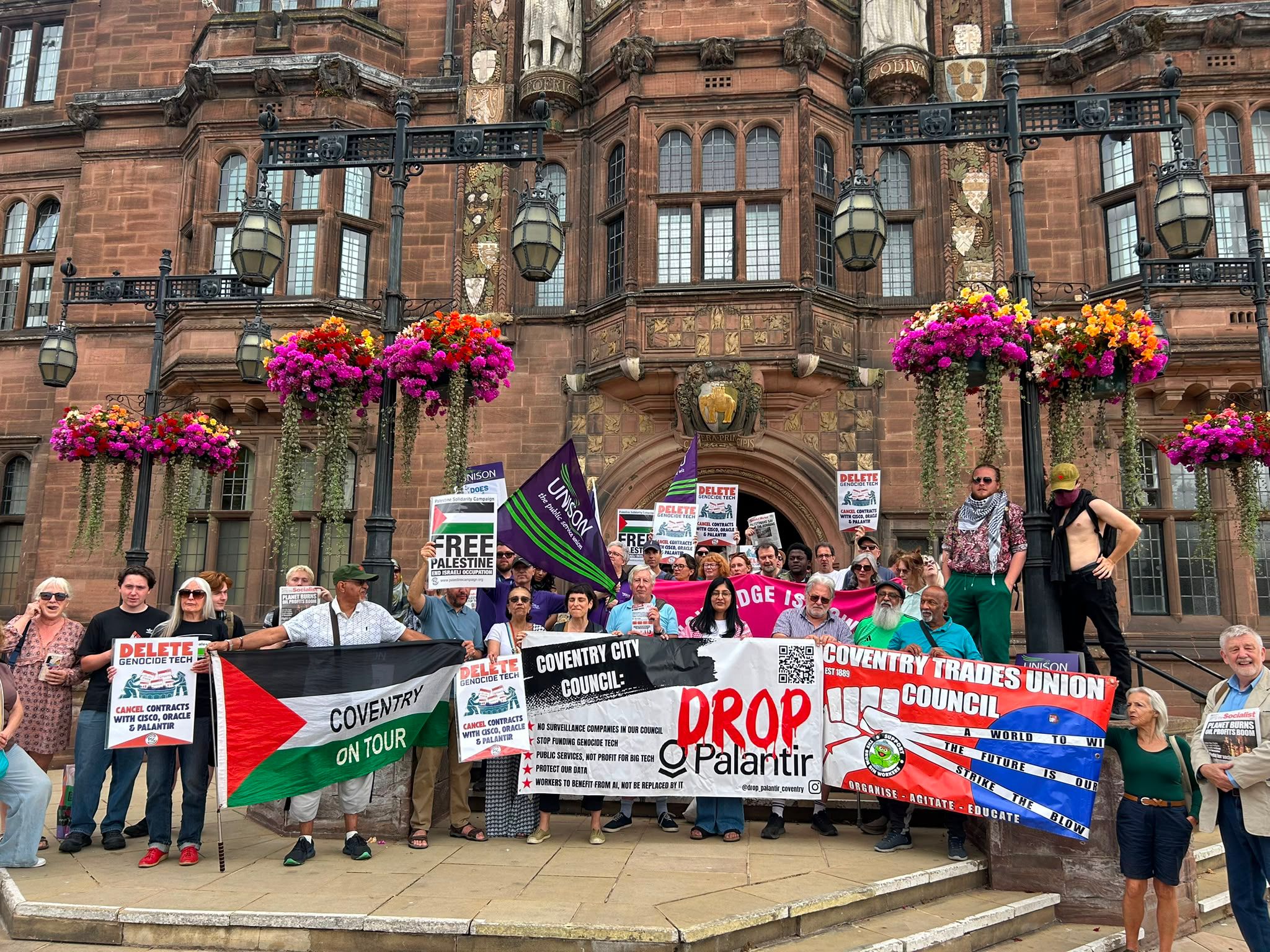 Campaigners holding Drop Palantir, trade union and Palestine solidarity banners on the steps of Coventry Council House